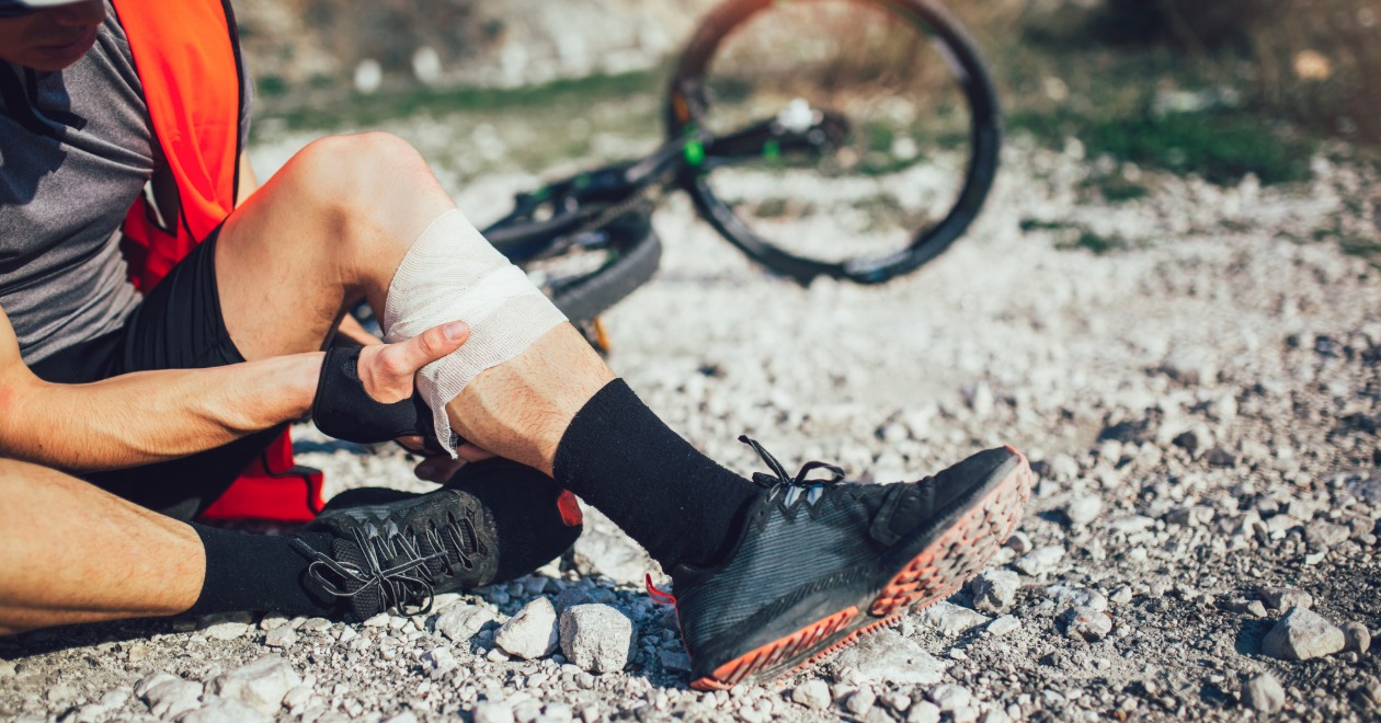 Injured cyclist with a bandaged knee beside a bicycle